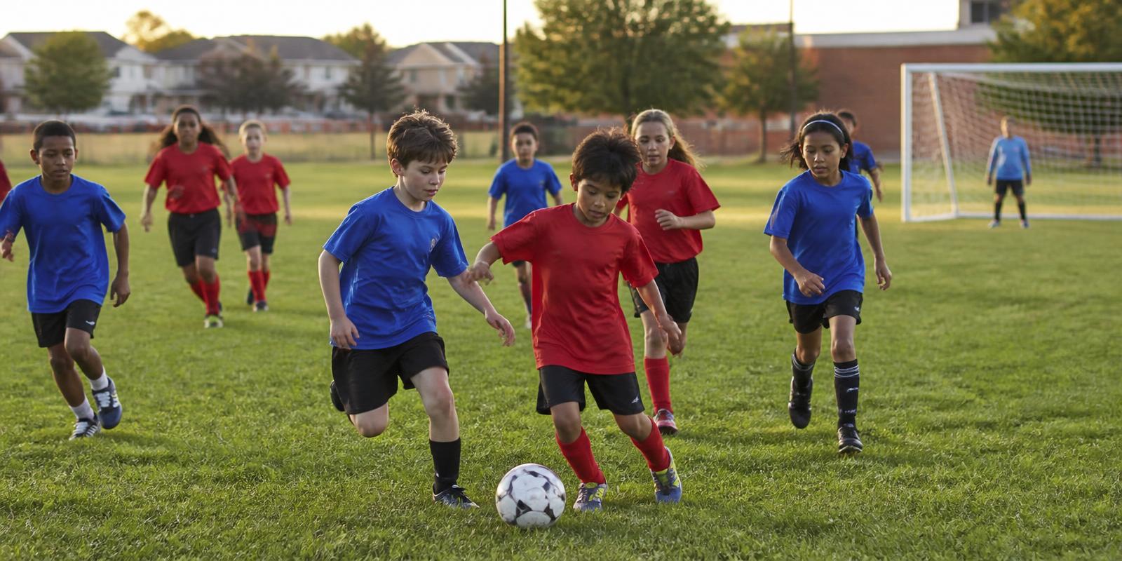 Kids in a community youth soccer game running for the ball on a neighbourhood grass field at golden hour